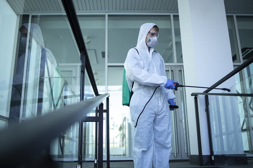 Unrecognizable person in white protection suit disinfecting public areas to stop spreading highly contagious virus