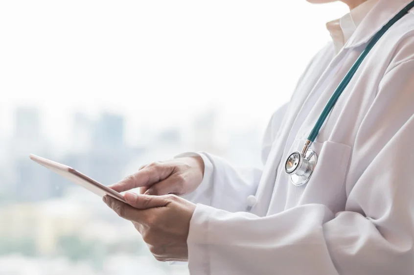 A doctor using a stethoscope around the neck and examining something on a screen with their hand – Healthcare Transformation with CloudPhysician