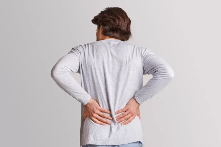 Man standing and clutching his lower back in discomfort, suggesting kidney pain.