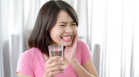 Person experiencing sharp tooth sensitivity while drinking cold water.