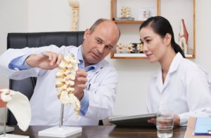 Spine specialist explaining cervical spondylosis using a cervical spine model during a consultation with a patient experiencing neck pain.